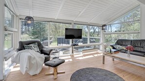 A spacious living room with a large TV, comfortable seating, and large windows offering a view of the outdoors.