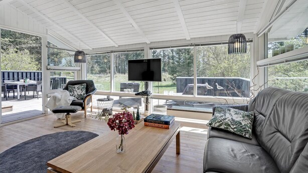 A spacious living room with a large window, a flat-screen TV, a sofa, a coffee table, and a dining area with outdoor seating.