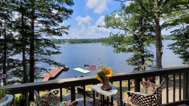 A deck with two metal chairs and a small table, overlooking a lake with boats and an American flag. - Glamorous lake house on a mountain lake in upstate New York (max of 8 guests) (East Berne)