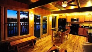 A wooden cabin interior with a dining area, kitchen, and large windows overlooking a deck. - Glamorous lake house on a mountain lake in upstate New York (max of 8 guests) (East Berne)