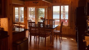 A wooden interior with a dining table and chairs, a ceiling fan, and large windows overlooking a lake. - Glamorous lake house on a mountain lake in upstate New York (max of 8 guests) (East Berne)