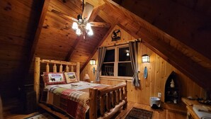 A cozy attic bedroom with a wooden ceiling, a bed with a quilt, a nightstand, a lamp, and a window with curtains. - Glamorous lake house on a mountain lake in upstate New York (max of 8 guests) (East Berne)