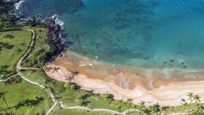 An aerial view of a coastal area with a sandy beach, clear blue waters, and lush greenery. - Stunning 2-bedroom Wailea Elua, walk to beach, ocean view!  (Kihei)