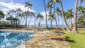 A poolside area with lounge chairs and umbrellas, palm trees, and a view of the ocean. - Stunning 2-bedroom Wailea Elua, walk to beach, ocean view!  (Kihei)