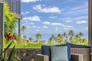 A balcony with wicker furniture and a view of the ocean and palm trees.