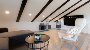 A modern loft bedroom with a sloped ceiling, a large bed, a seating area with a sofa and armchair, a small round table with plants, and built-in shelving. - Nice home in Slunj with swimming pool (Slunj)