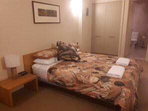 Une chambre d’hôtel avec un lit, une table de chevet avec une lampe, un tableau encadré au mur et une porte donnant sur une salle de bain.