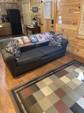 Una sala acogedora con un sofá, un tapete estampado y paredes de madera.