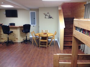 A room with a wooden dining table, four chairs, a TV mounted on the wall, a door, and a staircase. - Family Adventure Cabin in Mammoth Cave Country - Hot Tub - Disc Golf - Sleeps 8 (Mammoth Cave)