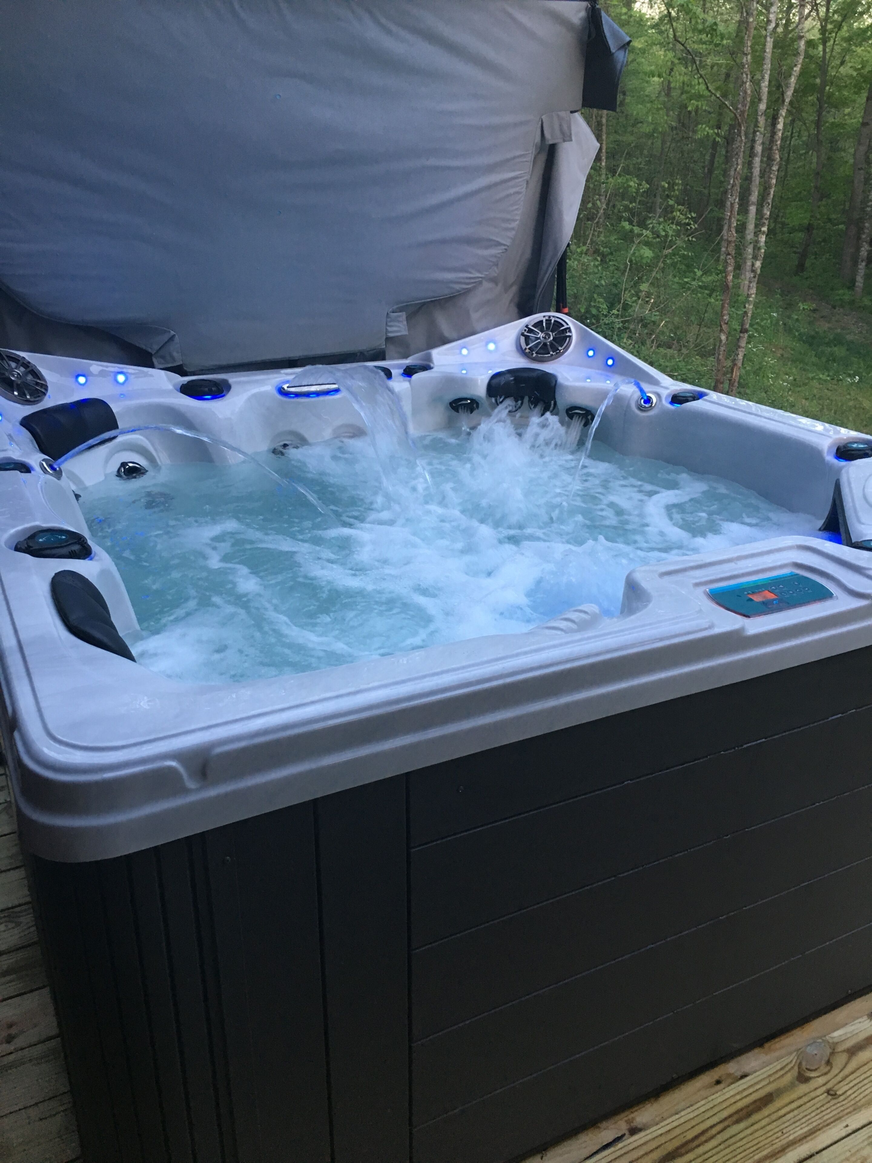 Un jacuzzi con múltiples chorros, rodeado por una terraza de madera y árboles.