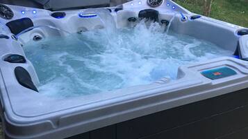 A hot tub with multiple jets, surrounded by a wooden deck and trees.