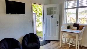 A room with a white door marked with a 'N', a flat-screen TV mounted on the wall, a dining table with two chairs, and two black bean bag chairs. - North Sunrise Studio - Retreat in Forks (Forks)