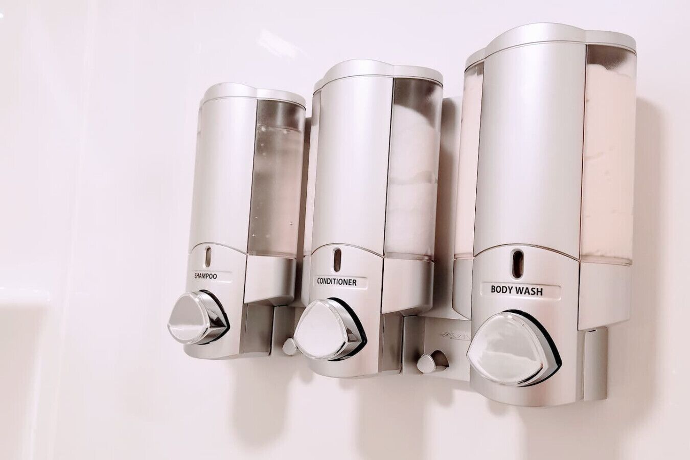 Une salle de bain avec des distributeurs muraux étiquetés « shampoing », « après-shampoing » et « gel douche ».
