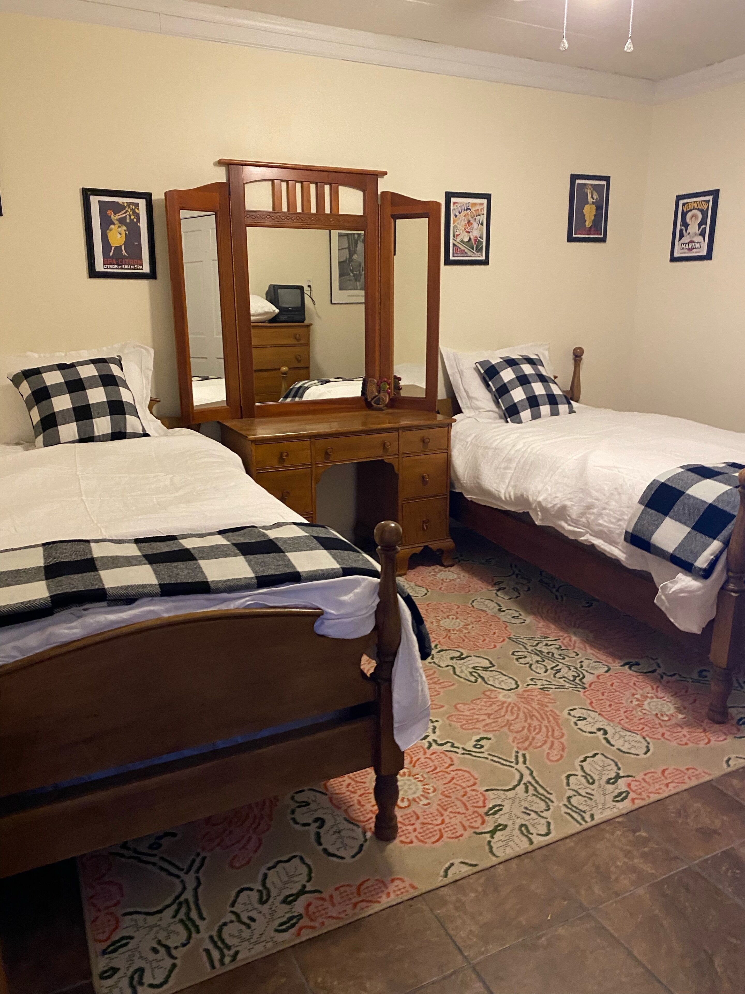 A bedroom with two single beds, a wooden dresser, a mirror, and a patterned rug.