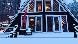 A multi-story chalet with large windows and a steeply pitched roof, surrounded by snow-covered trees.