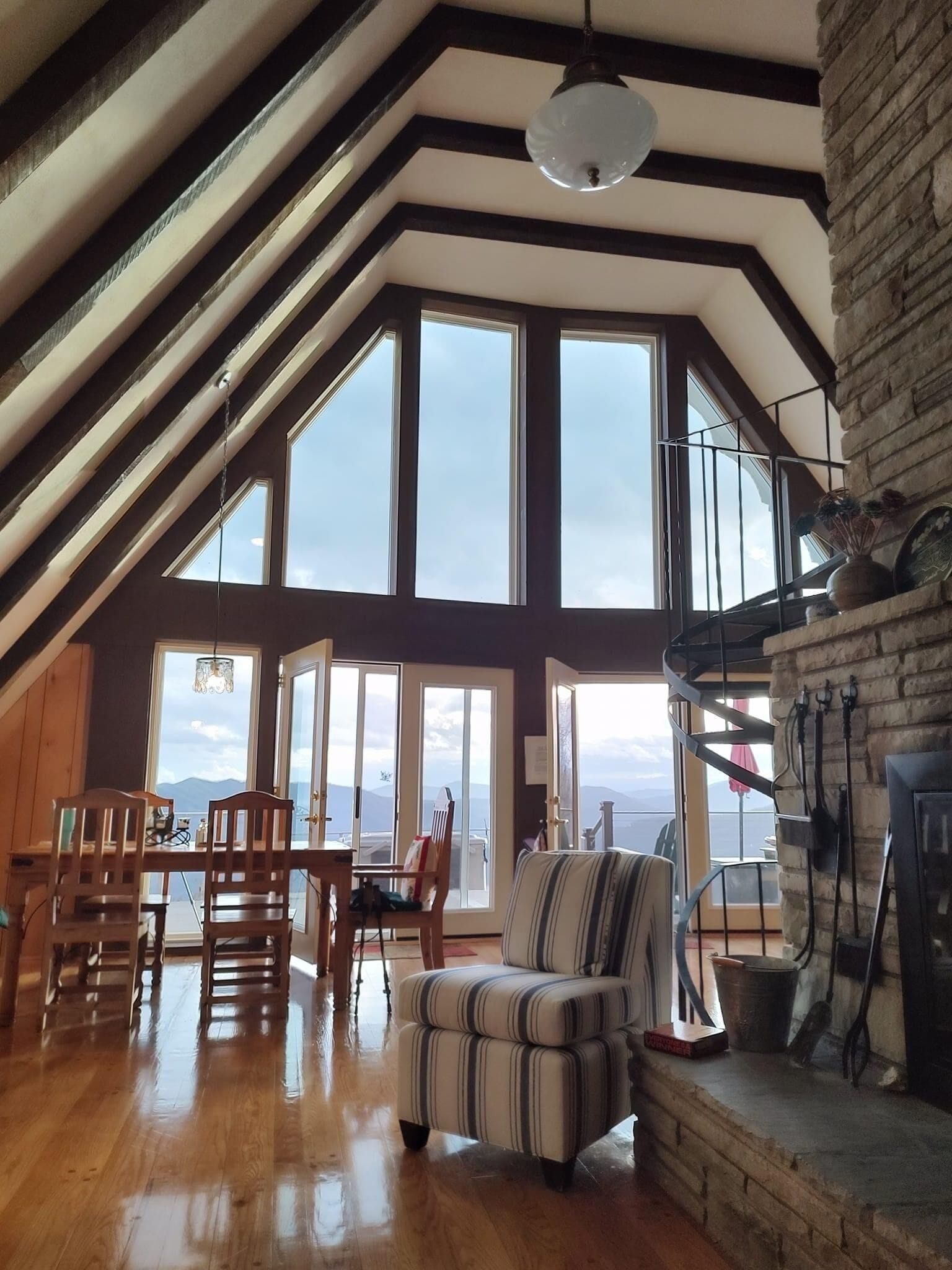 Un loft spacieux avec de hauts plafonds, de grandes fenêtres offrant une vue panoramique, un coin repas avec des meubles en bois et un coin salon confortable agrémenté d’un fauteuil à rayures.