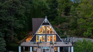 A modern house with a large deck, surrounded by dense forest.
