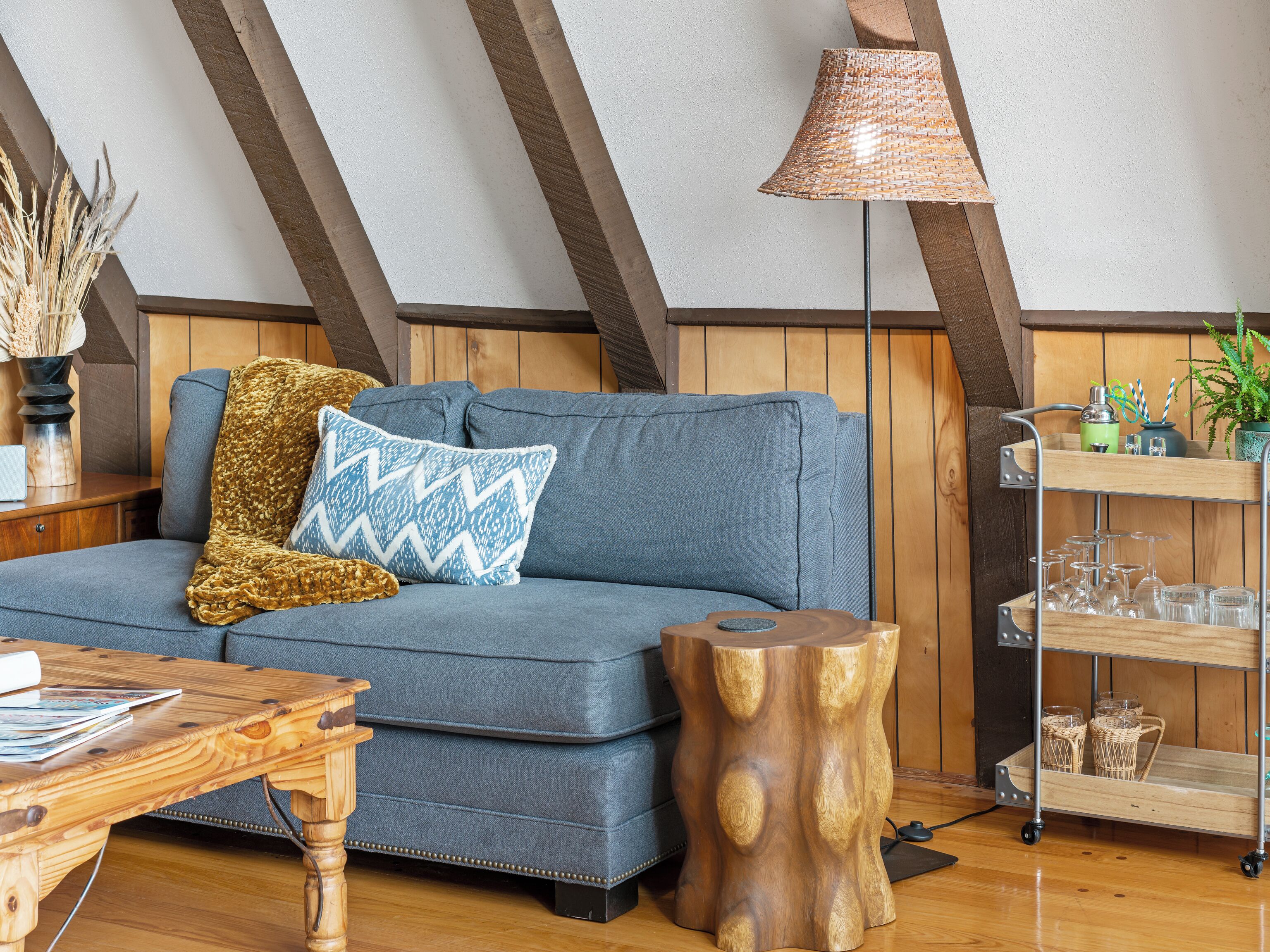 Un acogedor espacio tipo loft con un sofá azul, una mesa de centro de madera, una lámpara y una pequeña mesita de noche.
