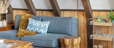 Un acogedor espacio tipo loft con un sofá azul, una mesa de centro de madera, una lámpara y una pequeña mesita de noche.