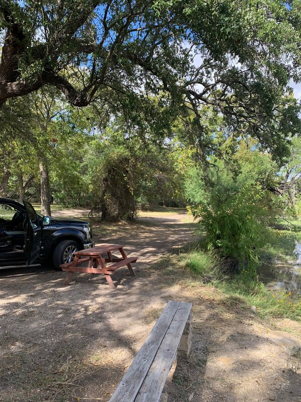 A campsite with a picnic table and a black vehicle parked nearby. - Relax and Enjoy Nature at Historic Fort Clark Springs (Brackettville)