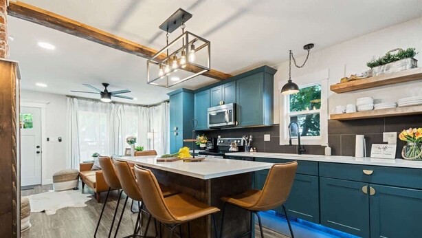 A modern kitchen with teal cabinets, a central island with bar stools, a ceiling fan, and pendant lighting. - Cozy Caldwell Retreat | Golf Course Views Near Downtown (Caldwell)