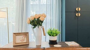 A room with a wooden table, a vase with flowers, a framed picture, and a cabinet with circular handles. - Cozy Caldwell Retreat | Golf Course Views Near Downtown (Caldwell)