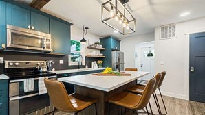 A modern kitchen with dark blue cabinets, stainless steel appliances, a central island with bar stools, and a pendant light. - Cozy Caldwell Retreat | Golf Course Views Near Downtown (Caldwell)