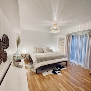 A bedroom with a wooden floor, a bed with a white and gray duvet, a hanging light fixture, and a window with sheer curtains. - 🌿5.0 Rating🌿 Sunny, spacious cozy retreat + firepit. World-class trails! (San Geronimo)