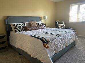Un dormitorio con una cama grande, una mesita de noche, una silla y una ventana con persianas.