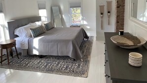 Ein modernes Schlafzimmer mit einem großen Bett, einer dunkelholznen Kommode, einem runden gewebten Korb und einer kleinen gewebten Tasse auf der Kommode.