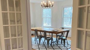Ein Essbereich mit Holztisch und -stühlen, einer Chandelierleuchtre und großen Fenstern.