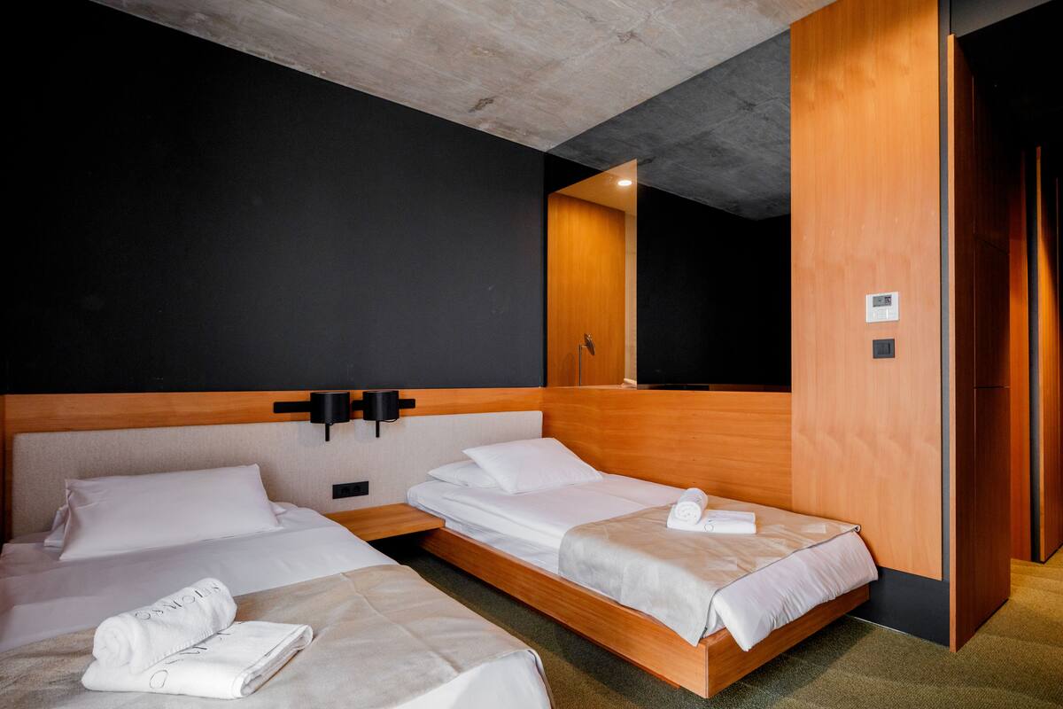 A hotel room with two beds, a wooden headboard, a black wall, and a wooden door.