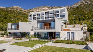 Una casa moderna de dos pisos con balcón, piscina y montañas al fondo.