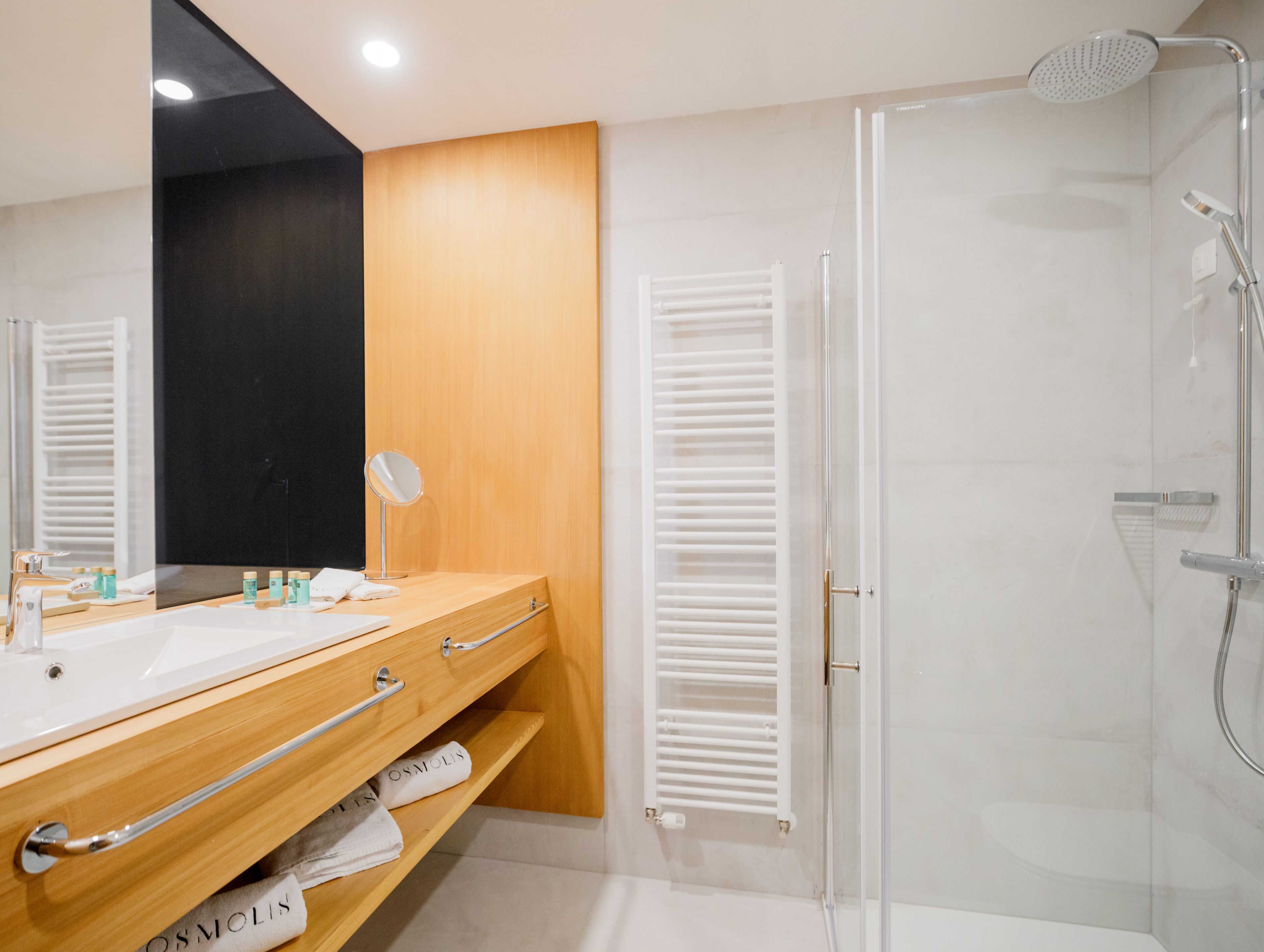 A modern bathroom with a wooden vanity, a large mirror, a shower with a glass door, and a towel rack.