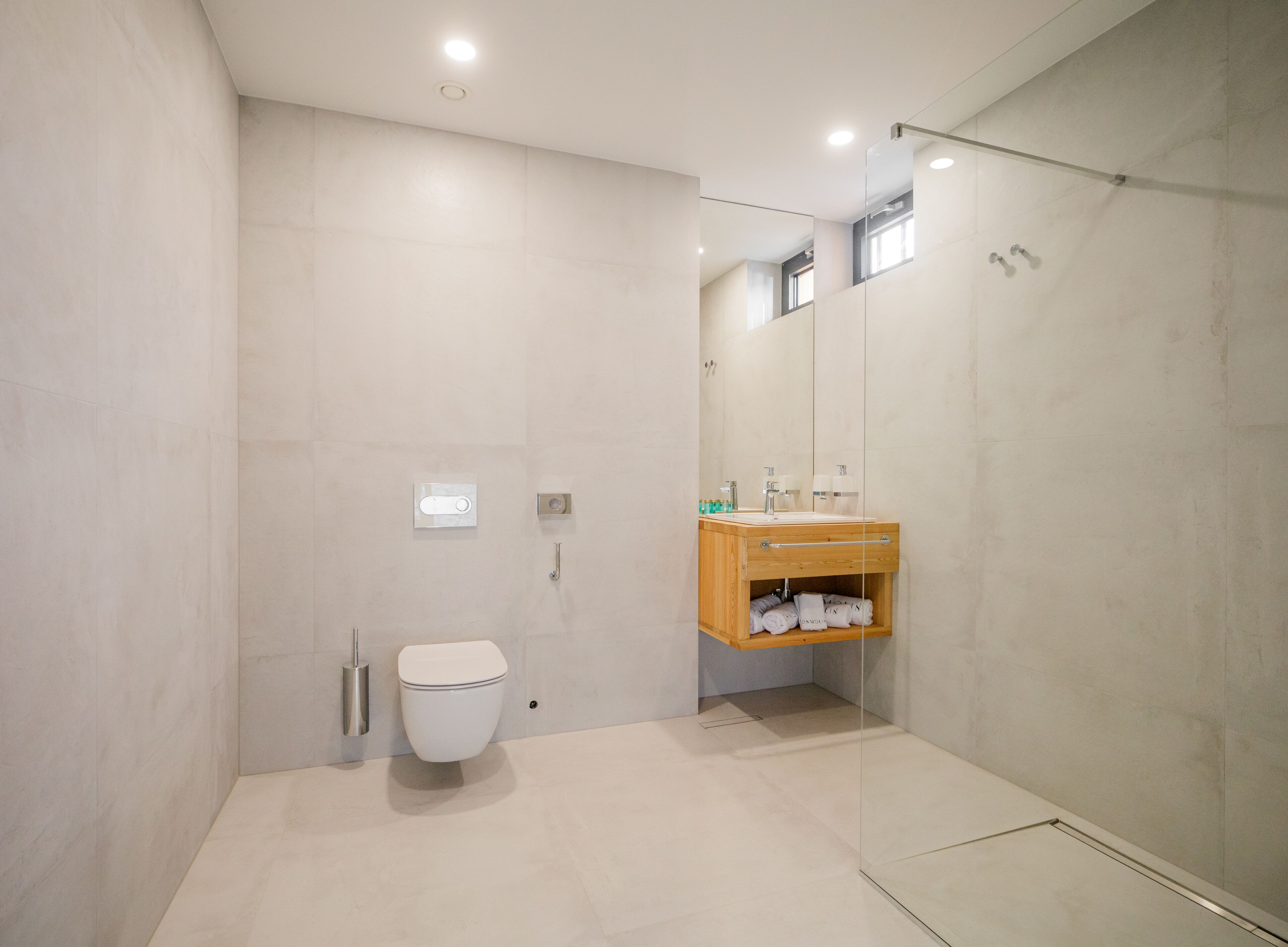 A modern bathroom with a toilet, a glass-enclosed shower, and a wooden vanity with a mirror.