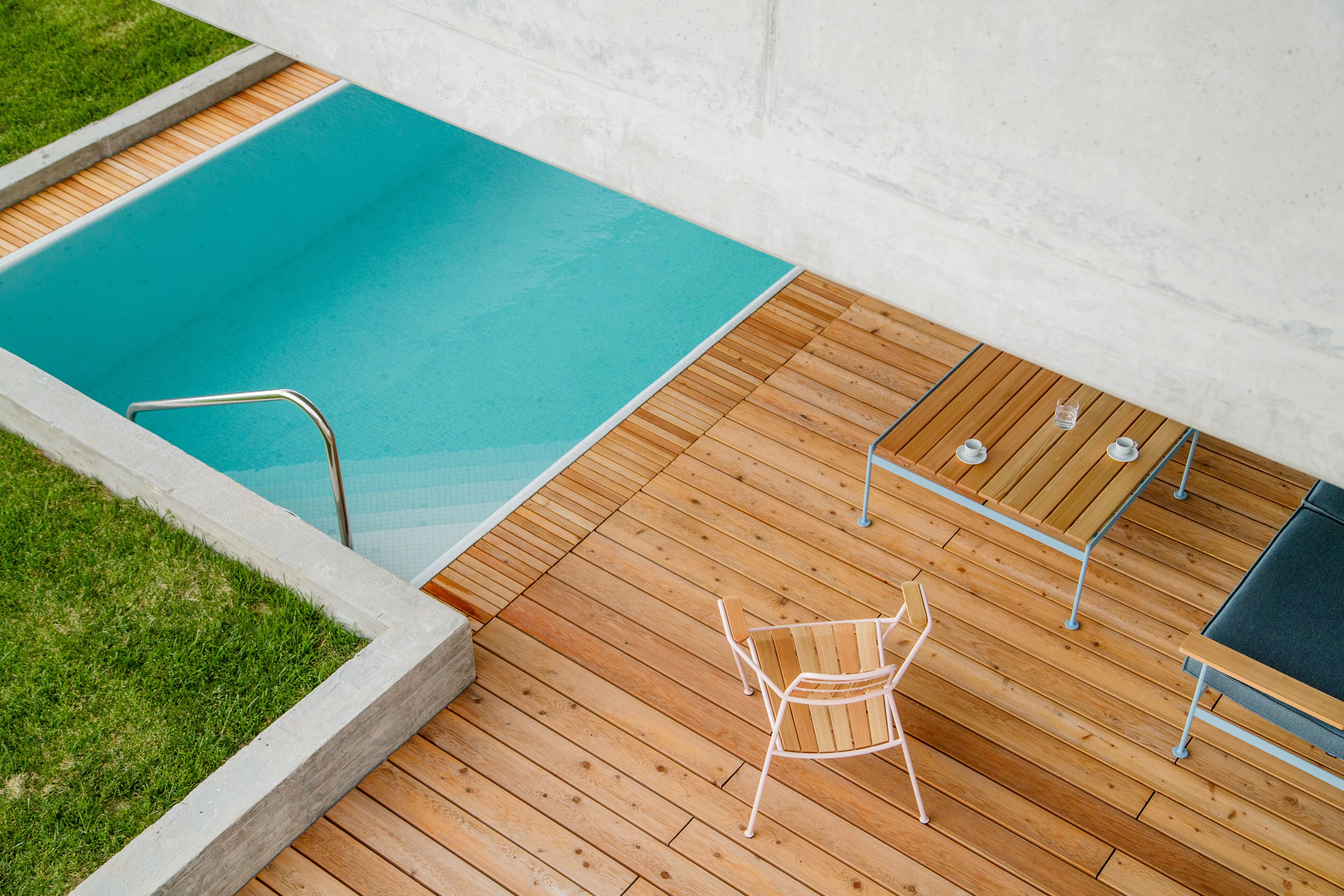 Une terrasse en bois avec une piscine, une chaise en métal et une table avec des chaises.