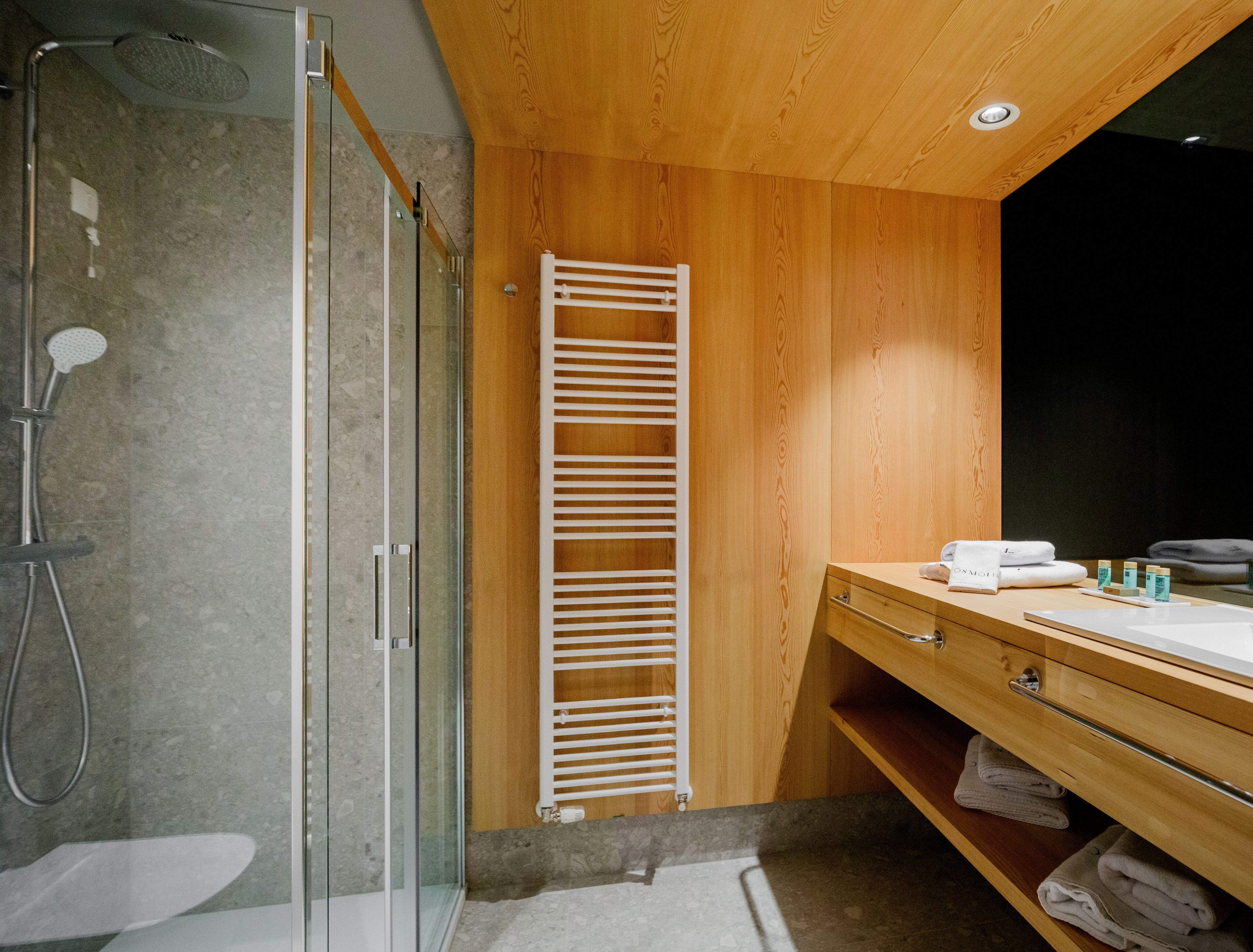 Un baño moderno con cabina de ducha de vidrio, paneles de madera, toallero integrado y tocador con espejo.