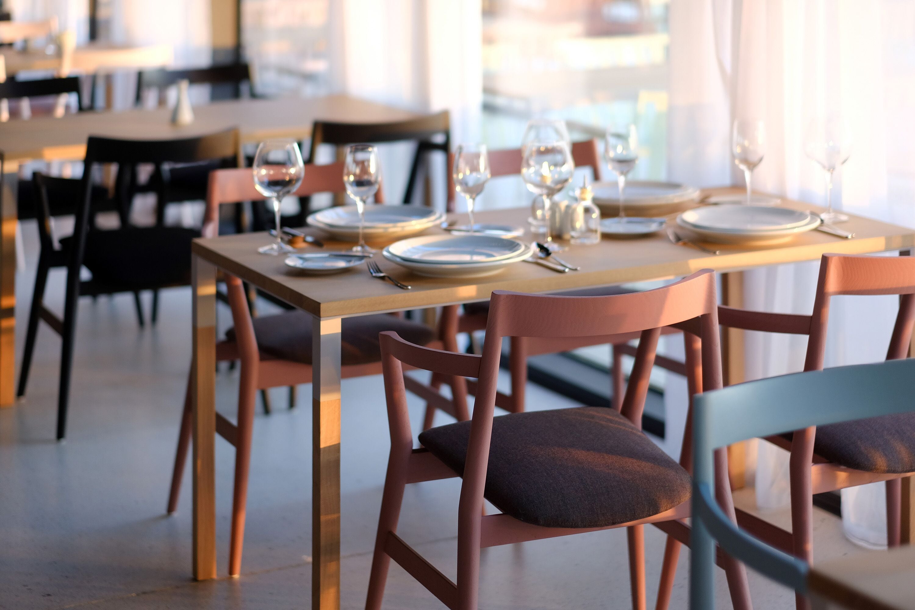A dining area with tables set for two, chairs, and wine glasses.