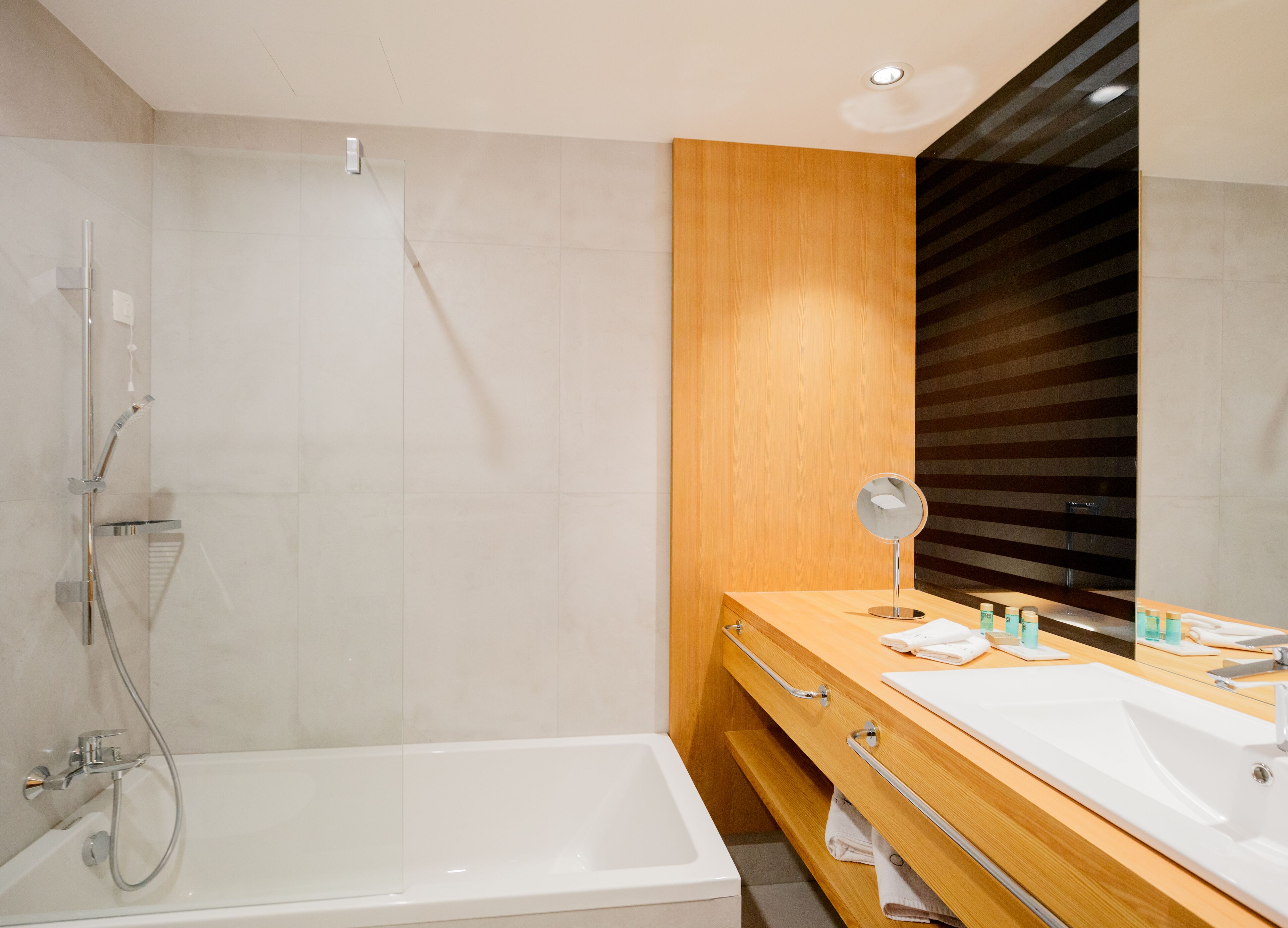 Une salle de bain moderne avec une baignoire, un meuble-lavabo en bois, un miroir et une douche.