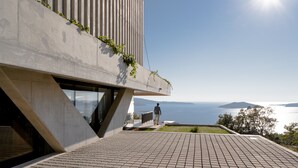Un edificio moderno con fachada de hormigón, una persona en una terraza y vista al mar.