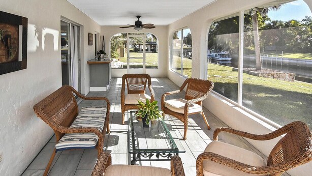 A covered patio with wicker furniture, a ceiling fan, and large windows overlooking a yard.
