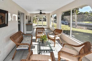 A covered patio with wicker furniture, a ceiling fan, and large windows overlooking a yard. - Stylish Canal Home with King Bed and Lanai  and Fishing dock (Punta Gorda)