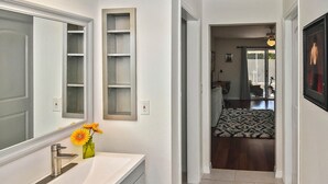 A bathroom with a white sink, mirror, and a shelf unit.
