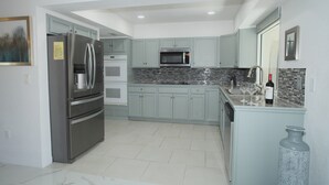A modern kitchen with stainless steel appliances, light green cabinets, and a tiled backsplash.