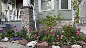 A house with a stone foundation, a porch with white railings, and a garden with pink tulips. - Spacious Historical Home by Parks, Shops, 4bd 2ba Save Weekly & monthly. (Buffalo)