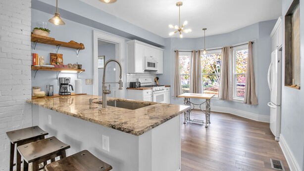A modern kitchen with a granite island, white cabinetry, and a dining area with a table and chairs. - Spacious Historical Home by Parks, Shops, 4bd 2ba Save Weekly & monthly. (Buffalo)