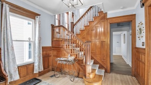 A wooden staircase with a handrail, a small table with a vase, and a rug on a wooden floor. - Spacious Historical Home by Parks, Shops, 4bd 2ba Save Weekly & monthly. (Buffalo)