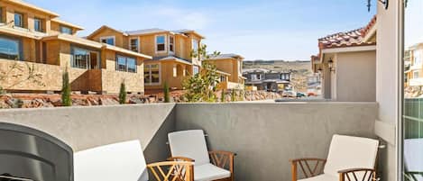 A balcony with outdoor seating, a grill, and a view of neighboring houses.