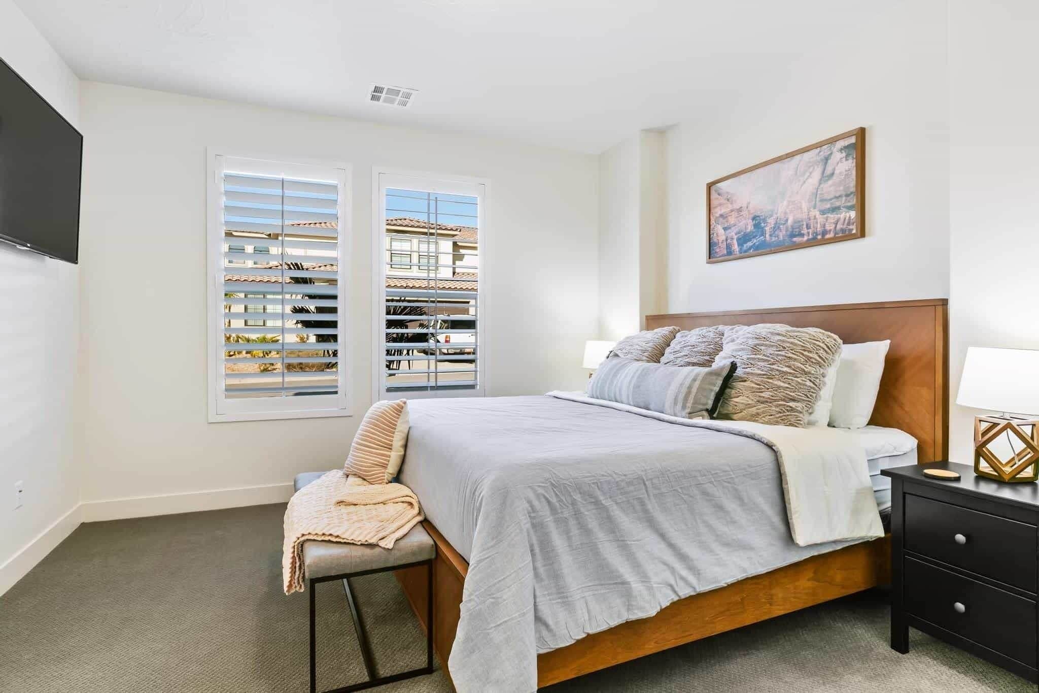 A bedroom with a bed, a chair, a nightstand, a TV, and a window with blinds.