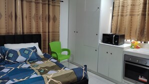 Une chambre avec un lit, un fauteuil vert, une armoire, un four à micro-ondes et une petite kitchenette équipée d’un four.